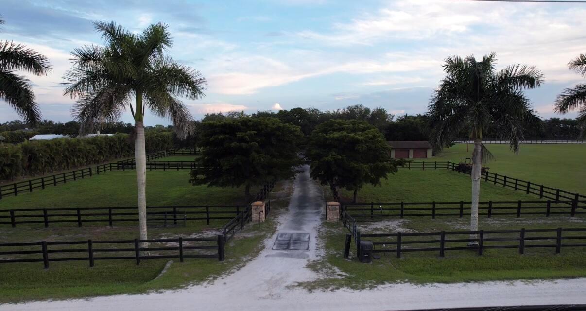 An aerial view of a gated driveway leading to a grassy field with palm trees — 16098 Deer Path Lane, Wellington FL 33470, WELLINGTON, FL