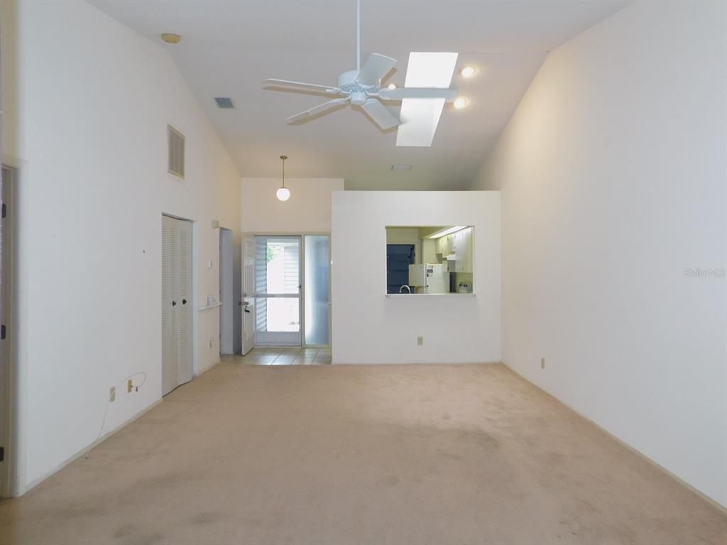 A living room with beige carpet, a vaulted ceiling, a ceiling fan, and a kitchen pass-through — 2496 ALHAMBRA COURT, CLEARWATER, FL