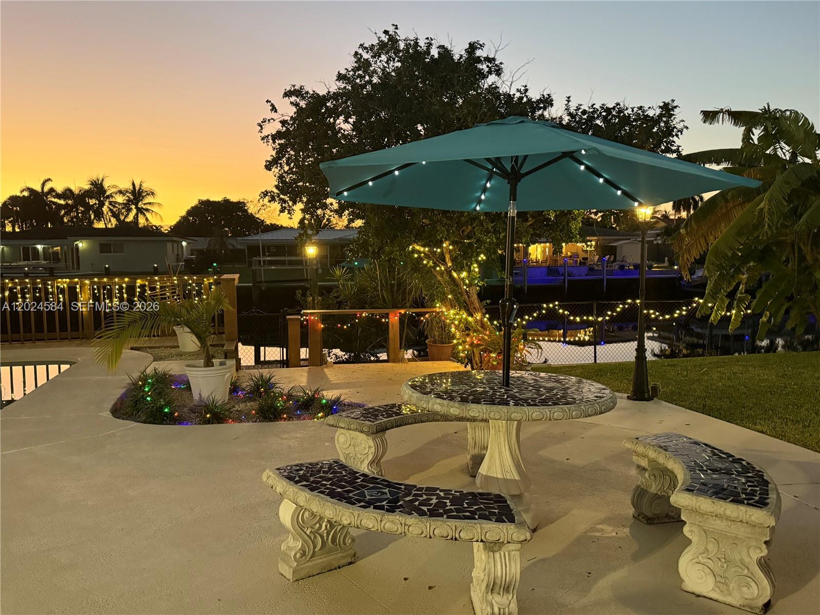 A patio features a mosaic table and benches under a lit umbrella at sunset — 411 SE 6th Ave, Pompano Beach FL 33060, POMPANO BEACH, FL