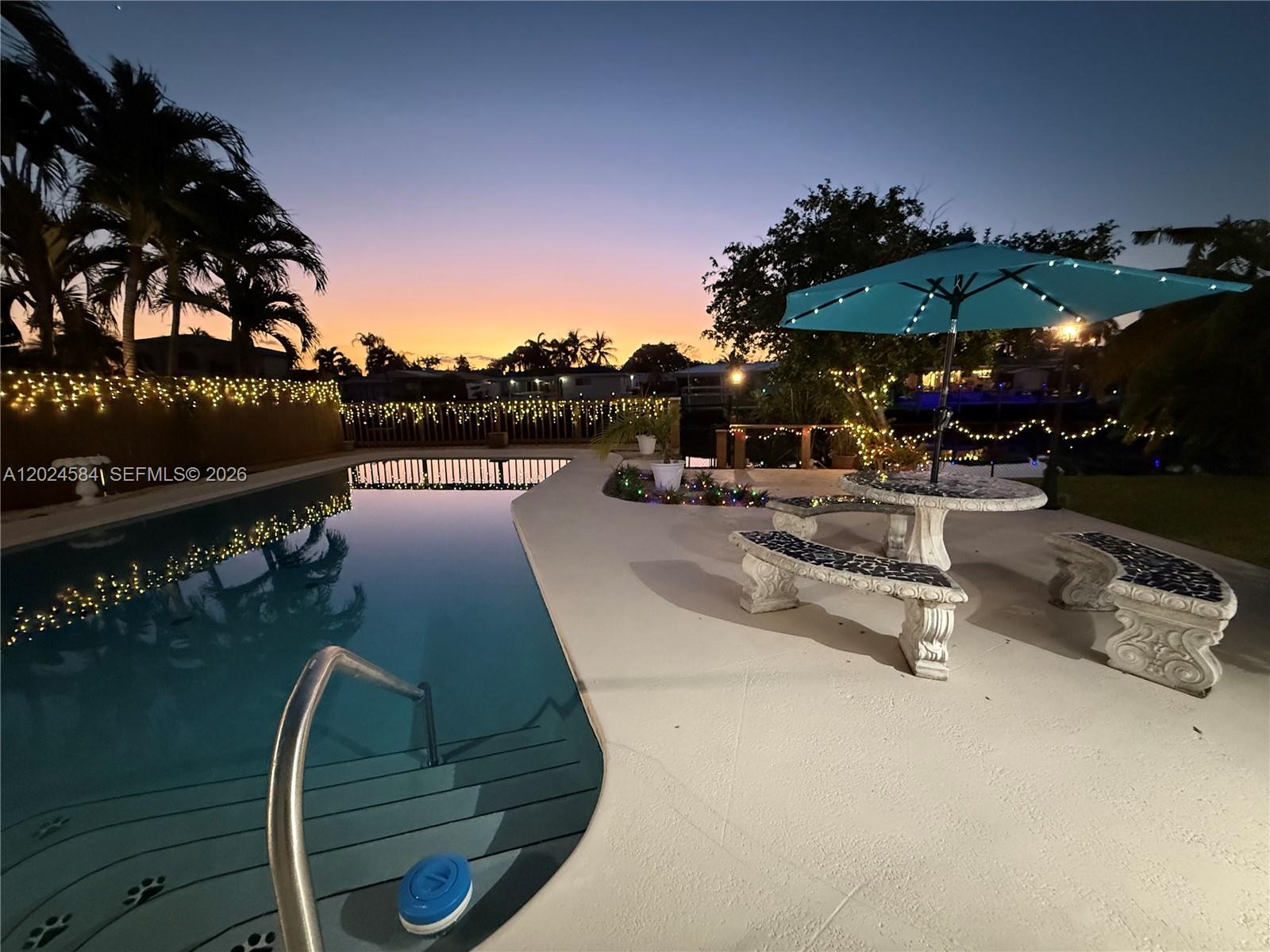 A swimming pool and patio area with a stone table and benches at sunset — 411 SE 6th Ave, Pompano Beach FL 33060, POMPANO BEACH, FL