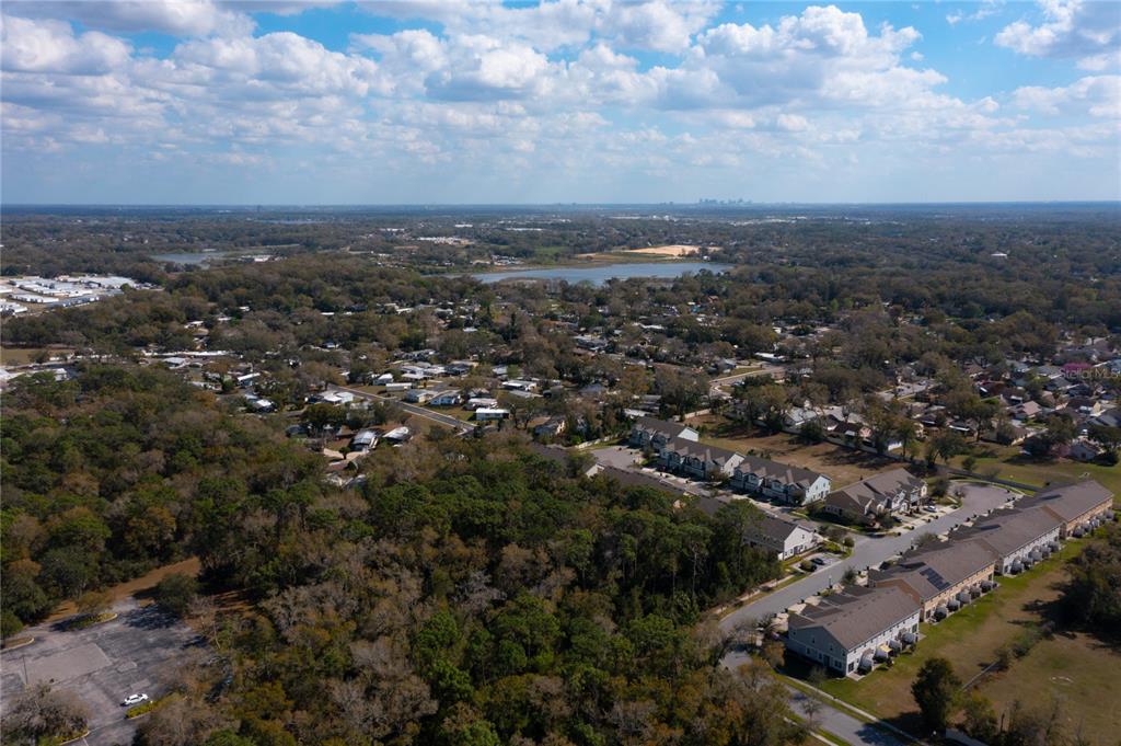 An aerial view shows a suburban neighborhood with townhomes, wooded areas, and a distant lake — E. 10th Street COUNTRYMEN COURT., APOPKA, FL