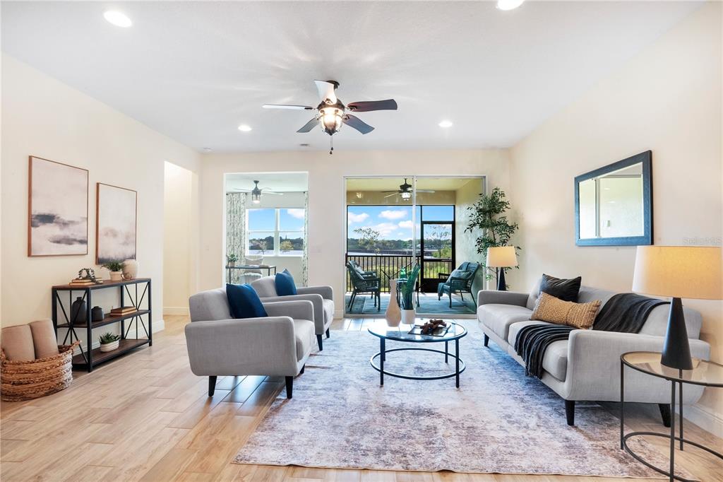 A bright living room features light wood-look flooring, gray furniture, and a sliding glass door — 9009 PALM KEY AVENUE, OLDSMAR, FL