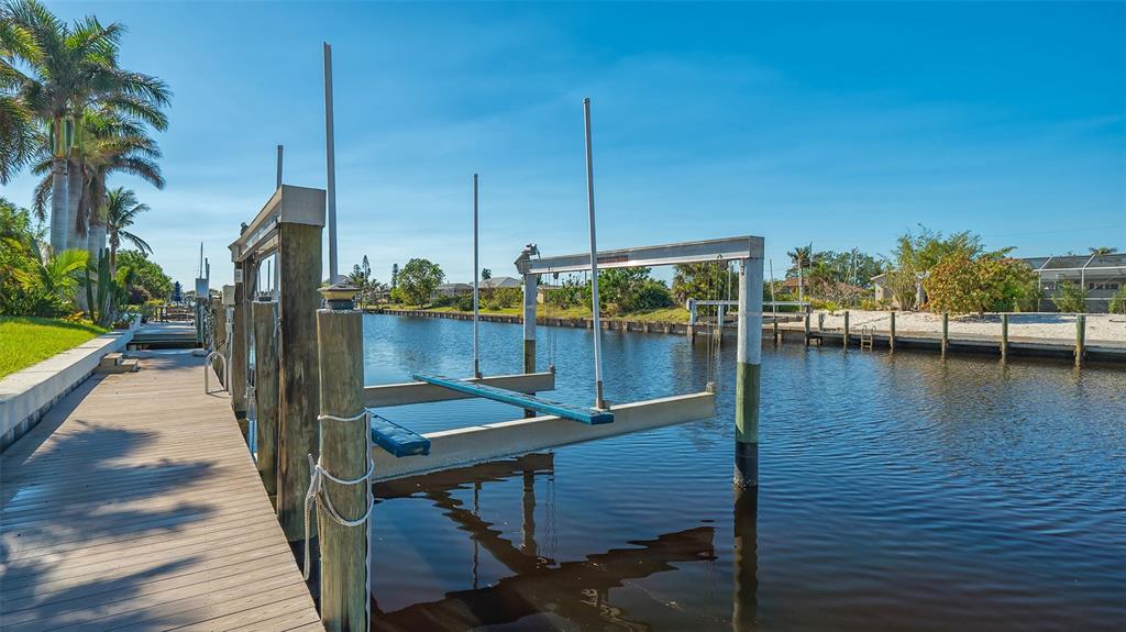A wooden dock features a boat lift extending over a canal with palm trees nearby — 108 ROSELLE COURT, PORT CHARLOTTE, FL
