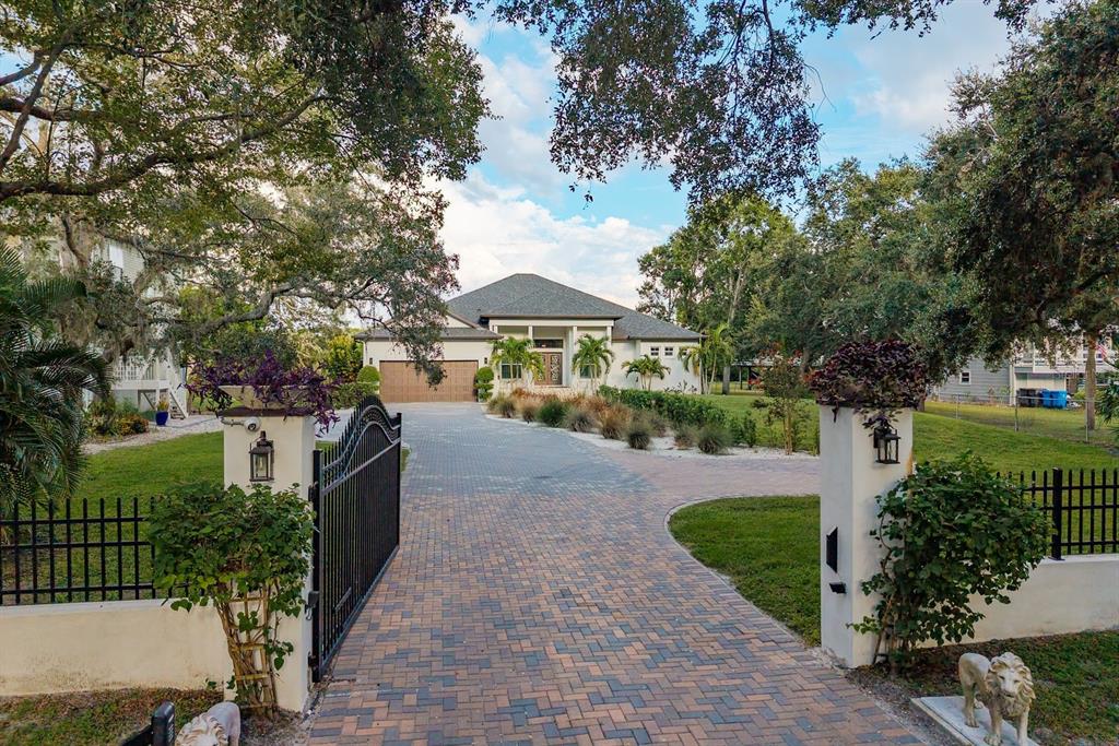 A paved driveway leads through a gated entrance to a single-story house with palm trees — 7811 BAY DRIVE UNIT A, TAMPA, FL
