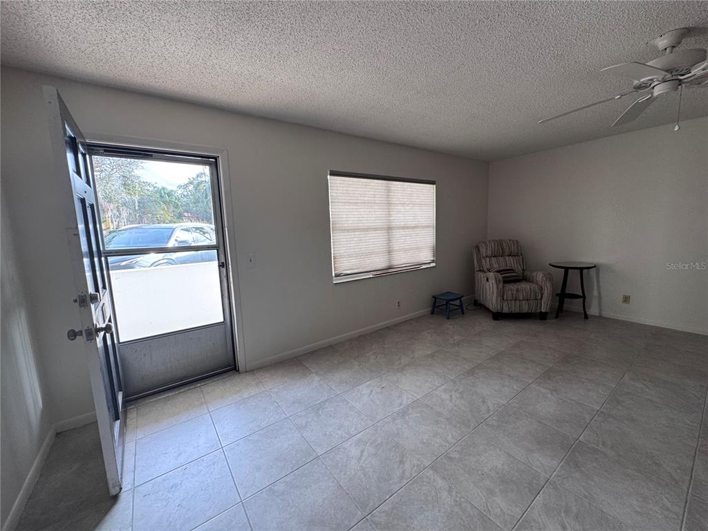 A room with light-colored tile flooring, a ceiling fan, a window, and an open door — 100 EL CAMINO DRIVE UNIT 111, WINTER HAVEN, FL