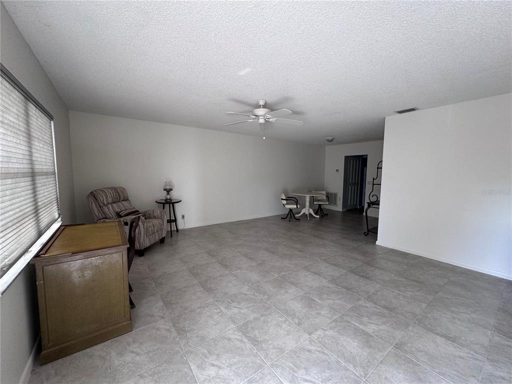 A spacious room features light gray tile flooring, white walls, and a ceiling fan — 100 EL CAMINO DRIVE UNIT 111, WINTER HAVEN, FL