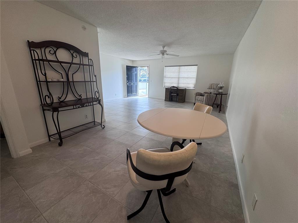 A dining area with tile flooring features a round table, chairs, and a metal baker's rack — 100 EL CAMINO DRIVE UNIT 111, WINTER HAVEN, FL