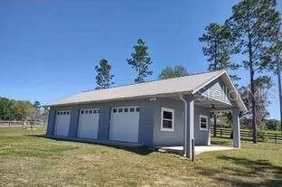 A detached gray garage with three white doors and a covered side porch — 13645 NW 222ND LANE, ALACHUA, FL