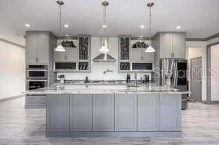 A modern kitchen features gray cabinetry, a large central island, and three hanging pendant lights — 13645 NW 222ND LANE, ALACHUA, FL