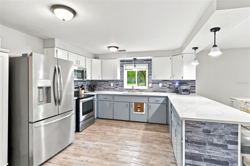 A kitchen features white upper cabinets, gray lower cabinets, stone-look backsplash, and stainless steel appliances — 1518 DICKENS ROAD, LAKE WALES, FL