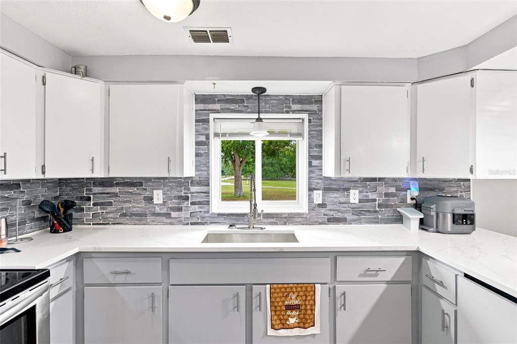 A kitchen features white upper cabinets, grey lower cabinets, a stone backsplash, and a window — 1518 DICKENS ROAD, LAKE WALES, FL