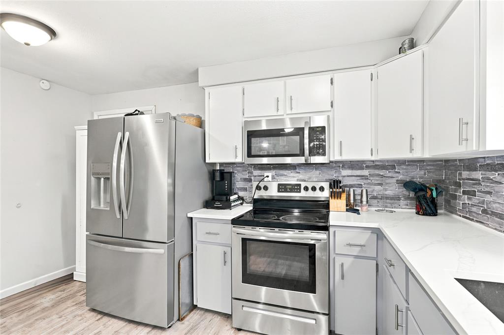 A kitchen features stainless steel appliances, white cabinets, and a gray stone-look tile backsplash — 1518 DICKENS ROAD, LAKE WALES, FL