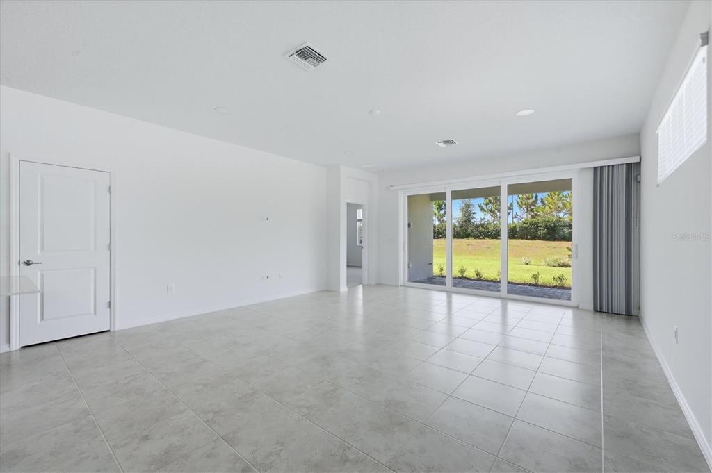 An empty living room with white walls, light tile flooring, and large sliding glass doors — 8113 STERNWAY ROAD, SARASOTA, FL