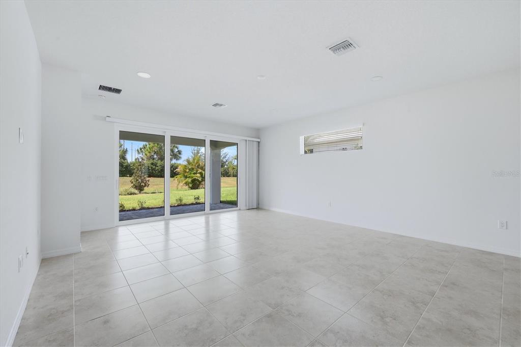 A bright, empty living room features white walls, light tile flooring, and large sliding glass doors — 8113 STERNWAY ROAD, SARASOTA, FL