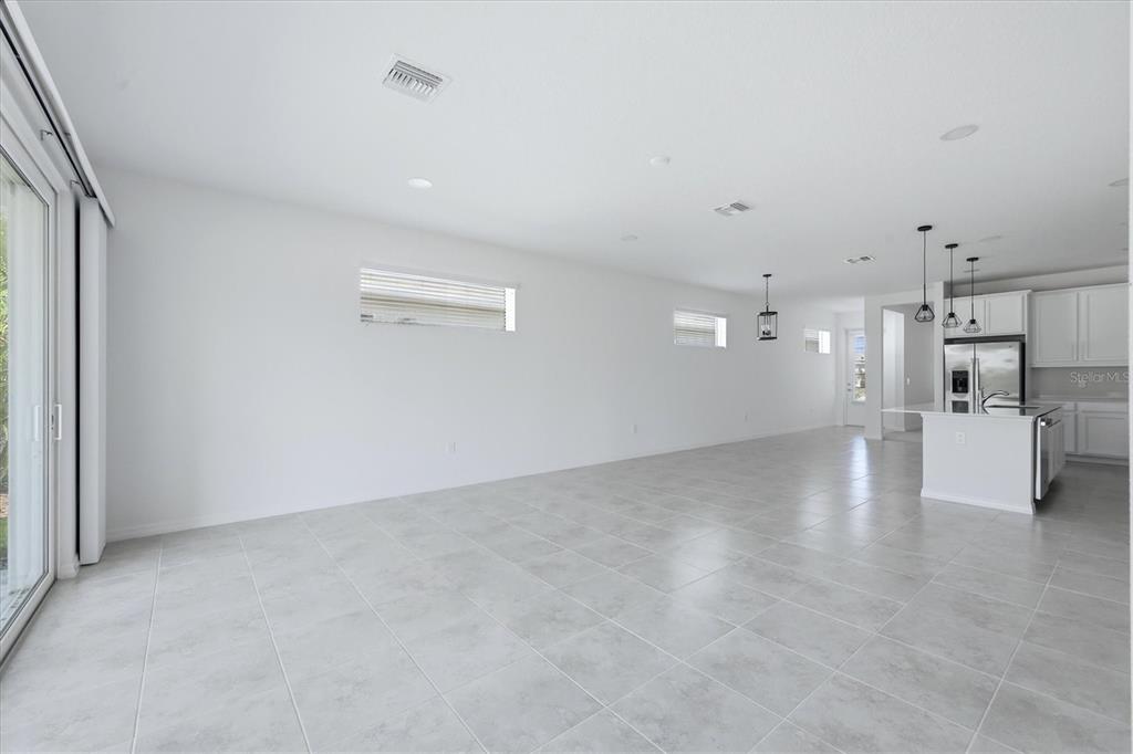 A bright, open-concept living area with white walls, tile flooring, and a modern kitchen — 8113 STERNWAY ROAD, SARASOTA, FL