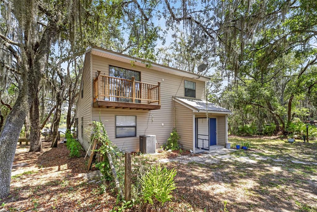 A two-story tan house with a wooden balcony and a blue door sits among trees — 273 NEAL ROAD, HAWTHORNE, FL