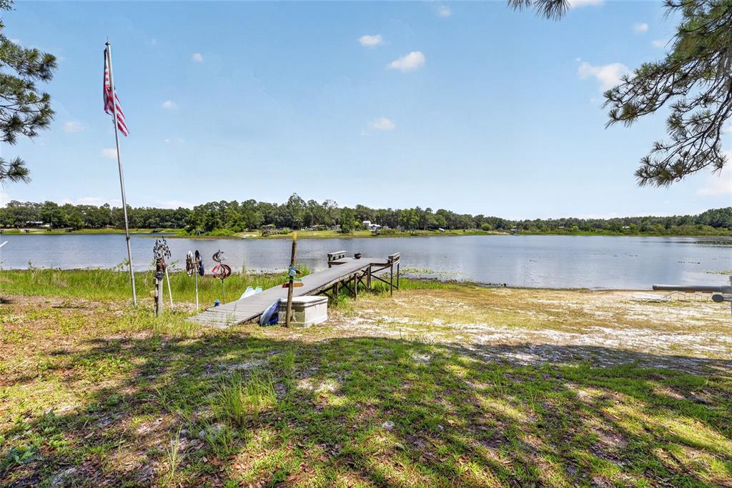 A wooden dock extends into a lake from a grassy, sandy shoreline under a blue sky — 273 NEAL ROAD, HAWTHORNE, FL