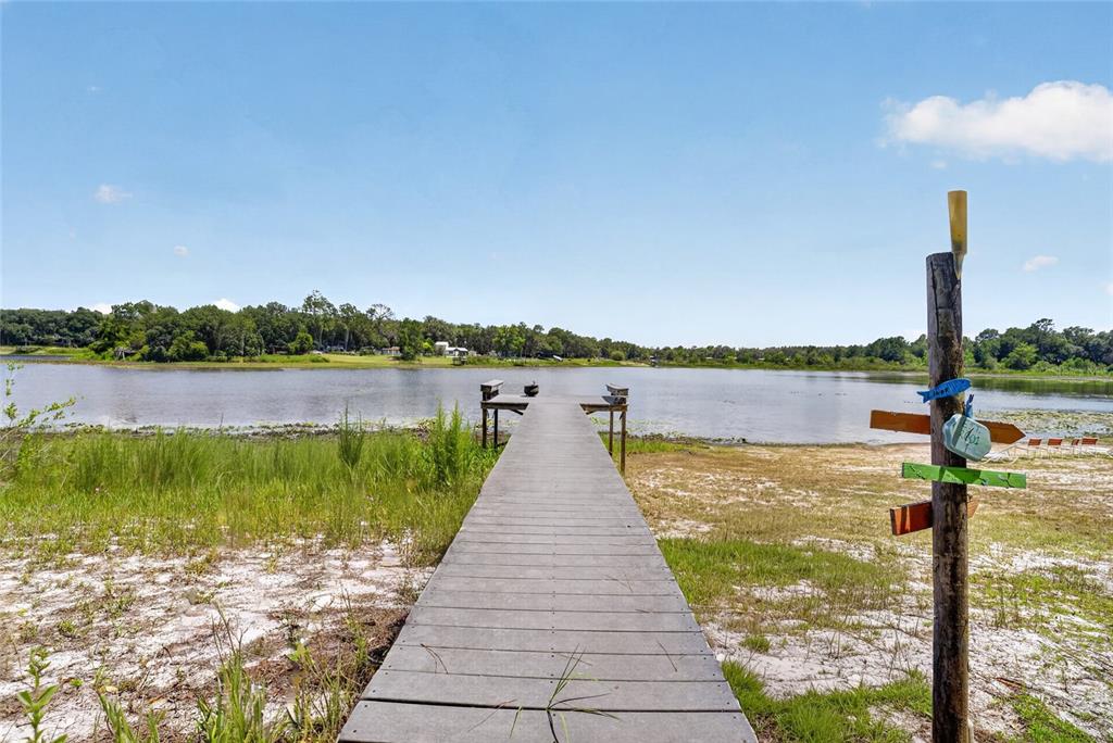 A wooden dock extends into a lake from a sandy shoreline with a signpost — 273 NEAL ROAD, HAWTHORNE, FL