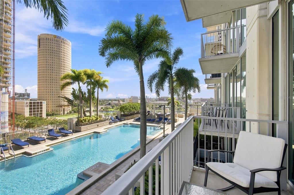A balcony overlooks a swimming pool with palm trees and a tall cylindrical building nearby — 777 N ASHLEY DRIVE UNIT 910, TAMPA, FL