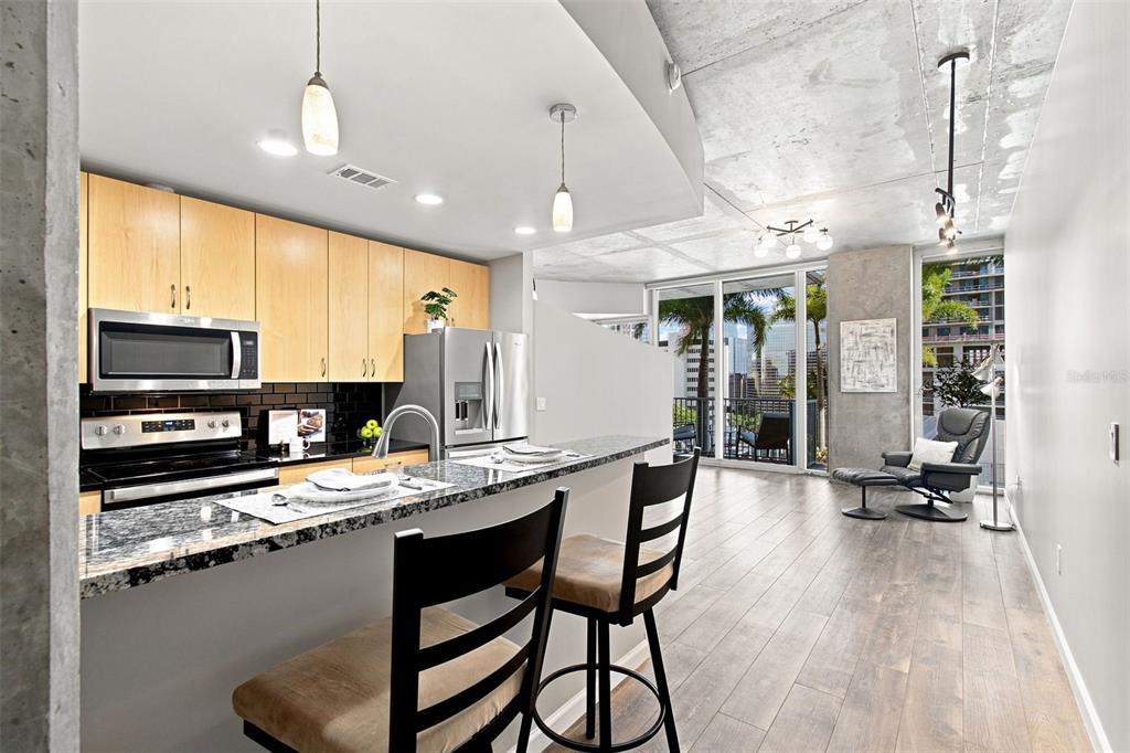 A modern kitchen with light wood cabinets and granite countertops overlooks an open-concept living area — 777 N ASHLEY DRIVE UNIT 910, TAMPA, FL