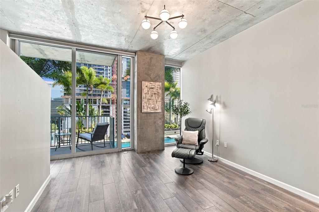 A modern living space features concrete ceilings, wood-look flooring, a recliner, and floor-to-ceiling windows — 777 N ASHLEY DRIVE UNIT 910, TAMPA, FL