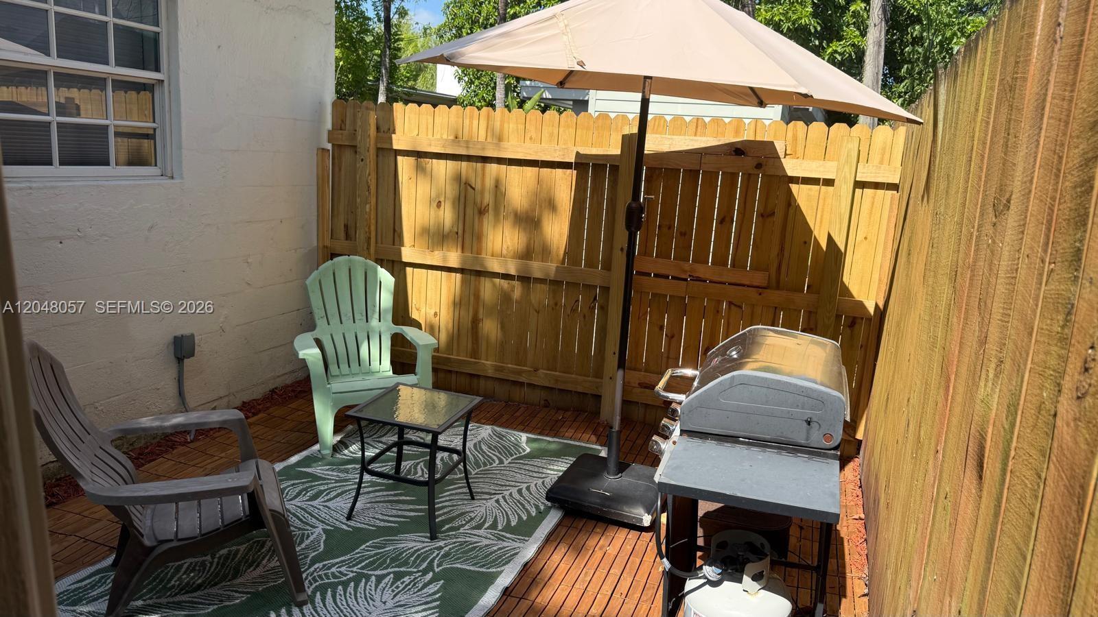 A small outdoor patio features a wooden fence, a grill, two chairs, and an umbrella — 3422 SW 25th St, Miami FL 33133, MIAMI, FL