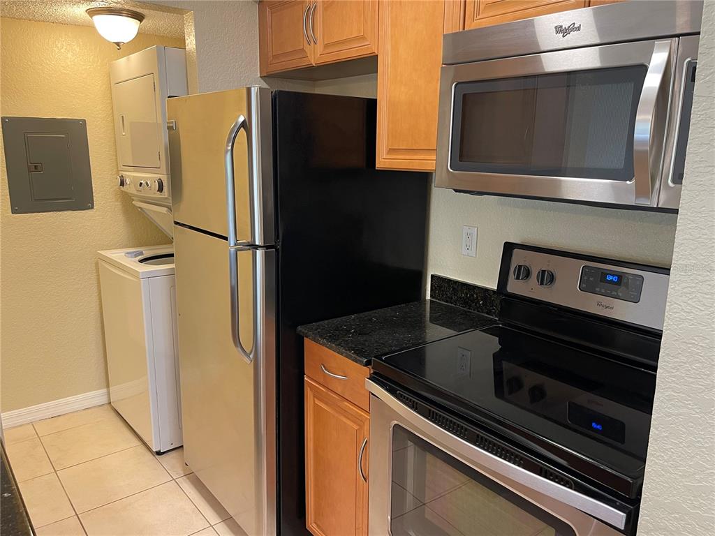 A kitchen with stainless steel appliances, wood cabinets, black countertops, and an adjacent laundry area — 500 BELCHER ROAD S UNIT 18, LARGO, FL