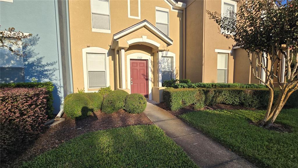 A tan two-story townhouse with a red front door and a concrete walkway — 1302 DENMAN COURT, WESLEY CHAPEL, FL