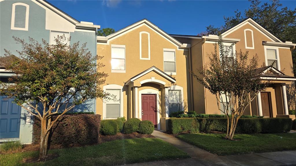 A row of three-story townhomes with tan and blue stucco exteriors and front landscaping — 1302 DENMAN COURT, WESLEY CHAPEL, FL