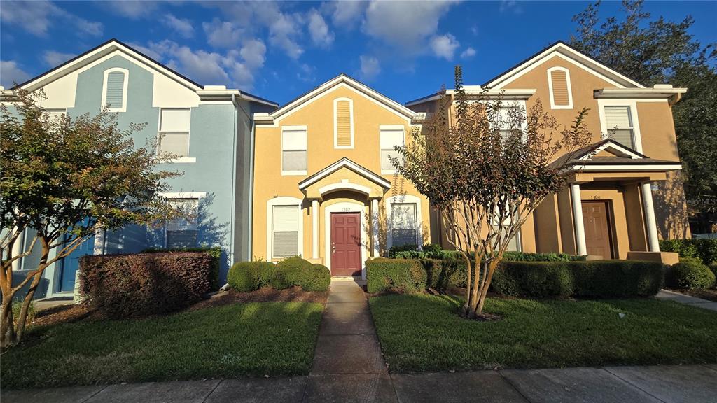 A row of three attached townhouses with blue, yellow, and tan stucco exteriors — 1302 DENMAN COURT, WESLEY CHAPEL, FL