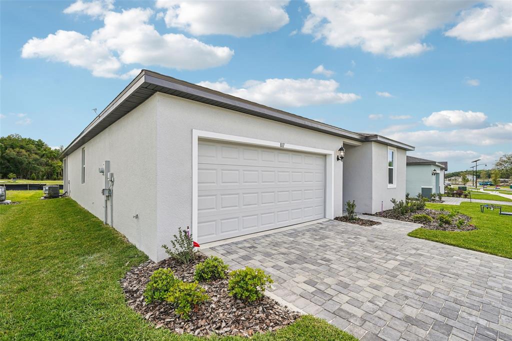 A single-story house with a light-colored stucco exterior, a two-car garage, and a paver driveway — 811 SUNSHOWER DRIVE, LADY LAKE, FL