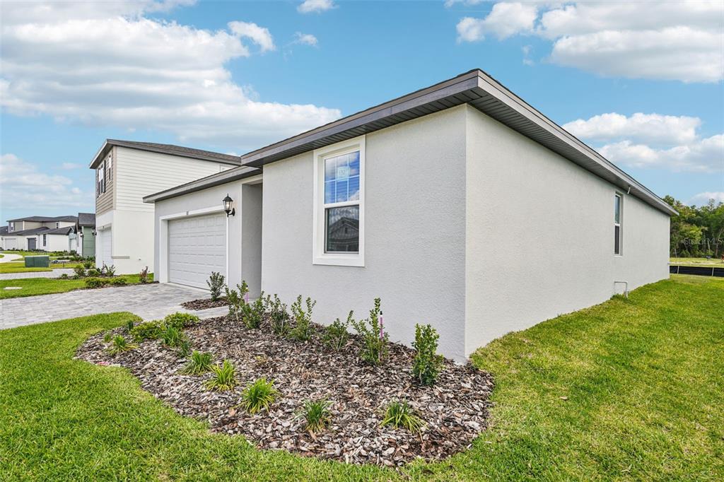 A side view of a single-story house with a garage, stucco siding, and landscaping — 811 SUNSHOWER DRIVE, LADY LAKE, FL