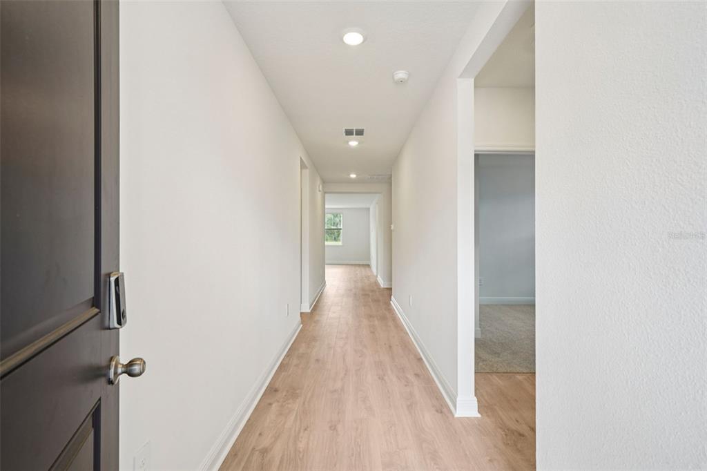 A hallway with light wood-look flooring leads from an entryway toward a distant window — 811 SUNSHOWER DRIVE, LADY LAKE, FL