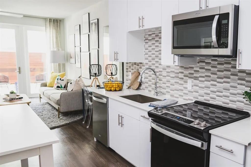 A modern kitchen with white cabinets and a patterned backsplash opens into a living area — 505-1 CHATHAM AVE AVENUE, ORLANDO, FL