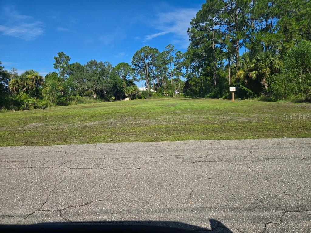 A vacant, grassy residential lot sits behind an asphalt road under a blue sky — 613 WILLARD AVENUE W, LEHIGH ACRES, FL
