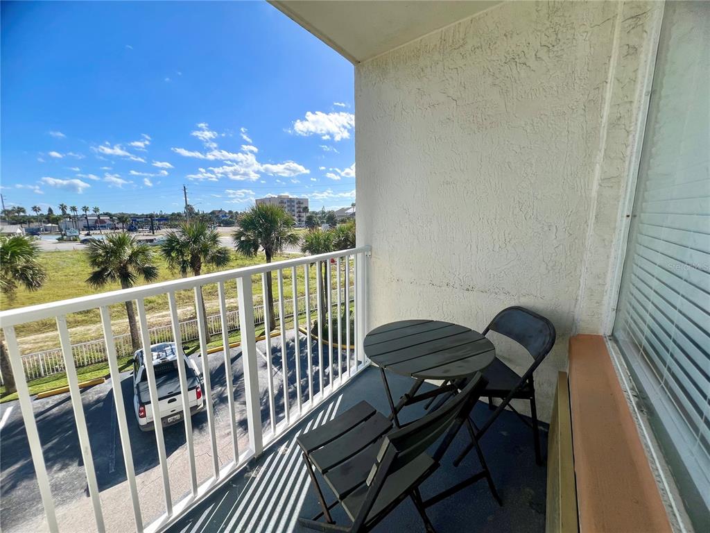 A balcony with a small table and two chairs overlooks a parking lot and palms — 935 S ATLANTIC AVENUE UNIT 303, DAYTONA BEACH, FL