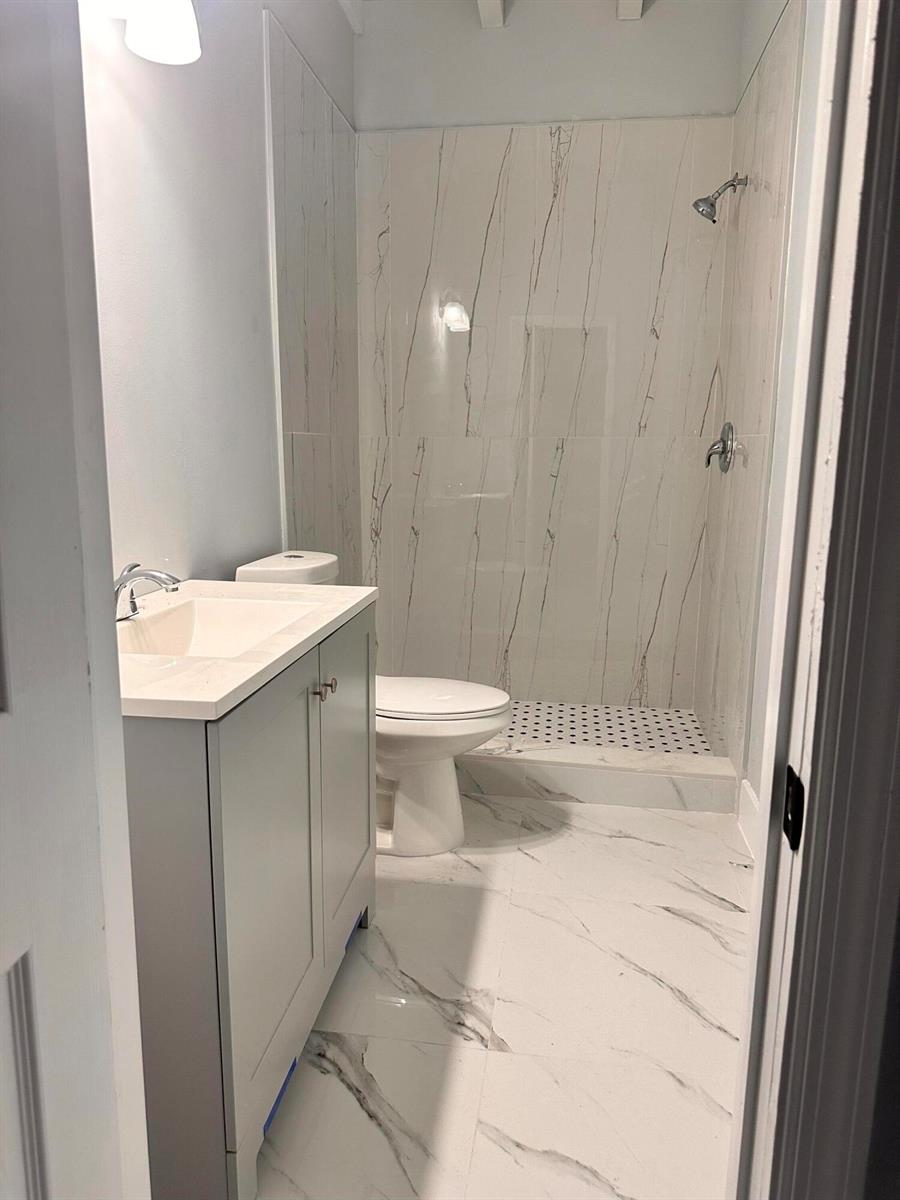 A small bathroom features a vanity, toilet, and a walk-in shower with marble-look tile — 3004 Alice Drive # 1, Palm Springs FL 33461, PALM SPRINGS, FL