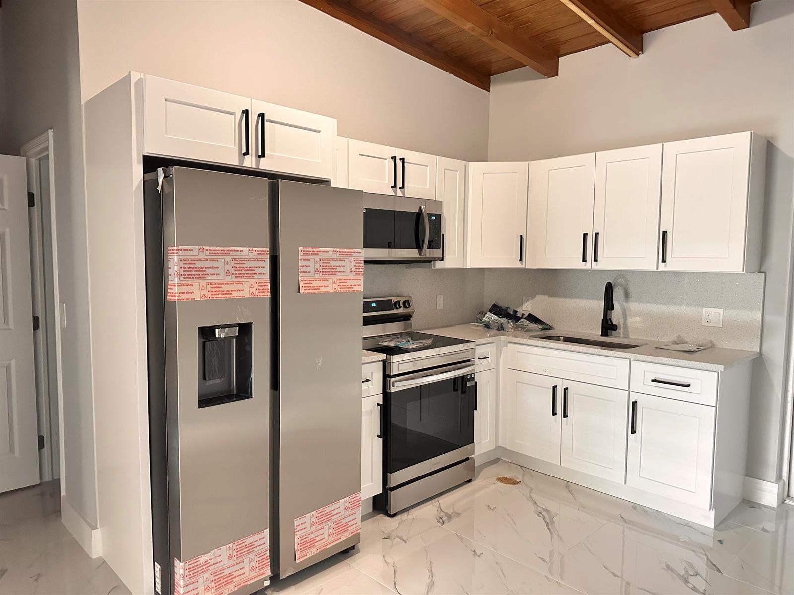 A kitchen features white cabinets, stainless steel appliances, a sink, and marble-patterned tile flooring — 3004 Alice Drive # 1, Palm Springs FL 33461, PALM SPRINGS, FL