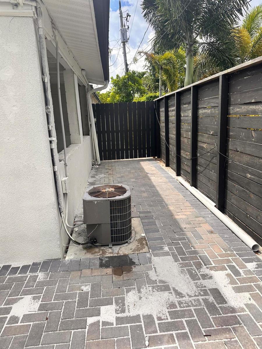 A side yard features a brick paver patio, an air conditioning unit, and a wooden fence — 3004 Alice Drive # 1, Palm Springs FL 33461, PALM SPRINGS, FL