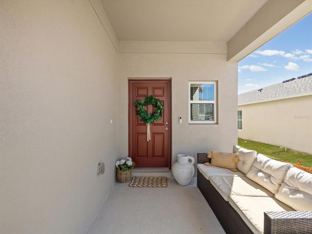 A covered porch features a red front door, a wicker sofa, and a white vase — 34110 SCARLET SAGE COURT, WESLEY CHAPEL, FL