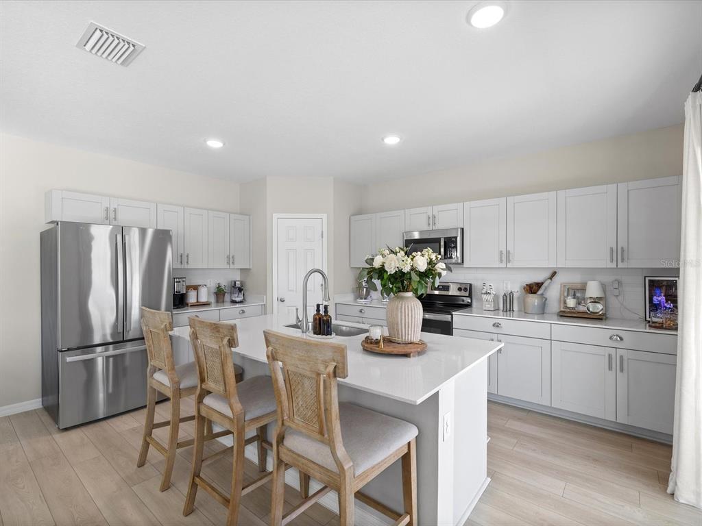 A modern kitchen features light gray cabinets, a white quartz island, and three wooden barstools — 34110 SCARLET SAGE COURT, WESLEY CHAPEL, FL