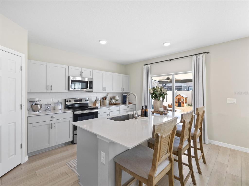 A kitchen features light gray cabinets, a white quartz island with bar seating, and stainless appliances — 34110 SCARLET SAGE COURT, WESLEY CHAPEL, FL