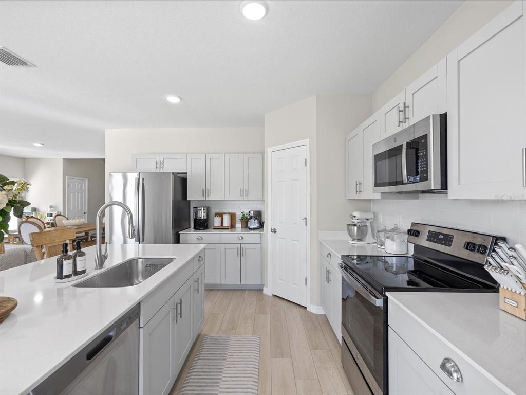 A modern kitchen features light gray cabinets, white countertops, stainless steel appliances, and wood-look flooring — 34110 SCARLET SAGE COURT, WESLEY CHAPEL, FL