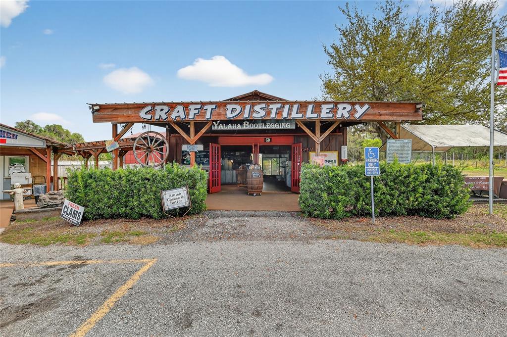 The exterior of a rustic craft distillery building features a wooden sign and gravel parking — 26921 BLOOMFIELD AVENUE, YALAHA, FL