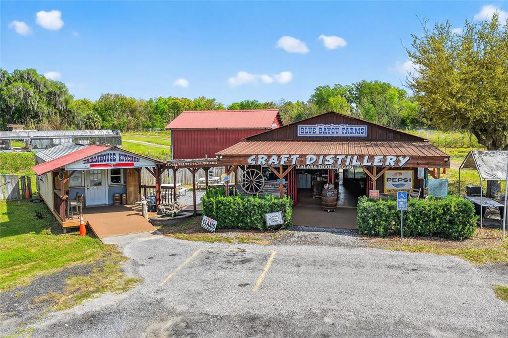 An exterior view shows a rustic farmhouse kitchen and a craft distillery with metal roofs — 26921 BLOOMFIELD AVENUE, YALAHA, FL