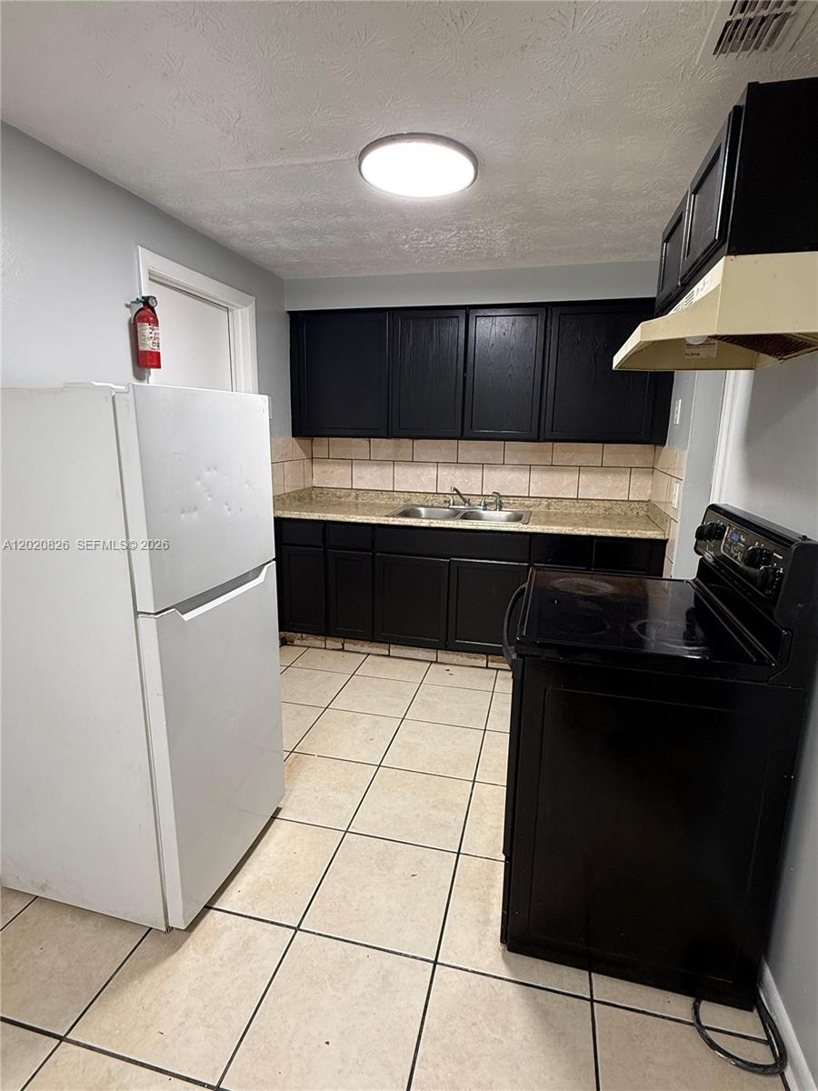 A kitchen features black cabinets, a white refrigerator, a black stove, and tiled flooring — 2644 West, Jacksonville FL 32209, JACKSONVILLE, FL