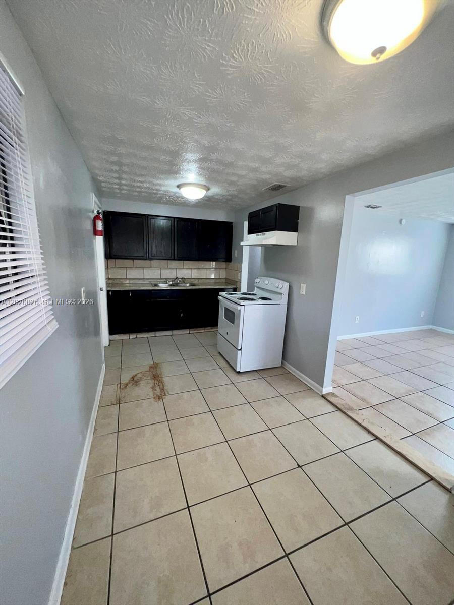 A kitchen with dark cabinets, a white stove, and light-colored tile flooring — 2644 West, Jacksonville FL 32209, JACKSONVILLE, FL