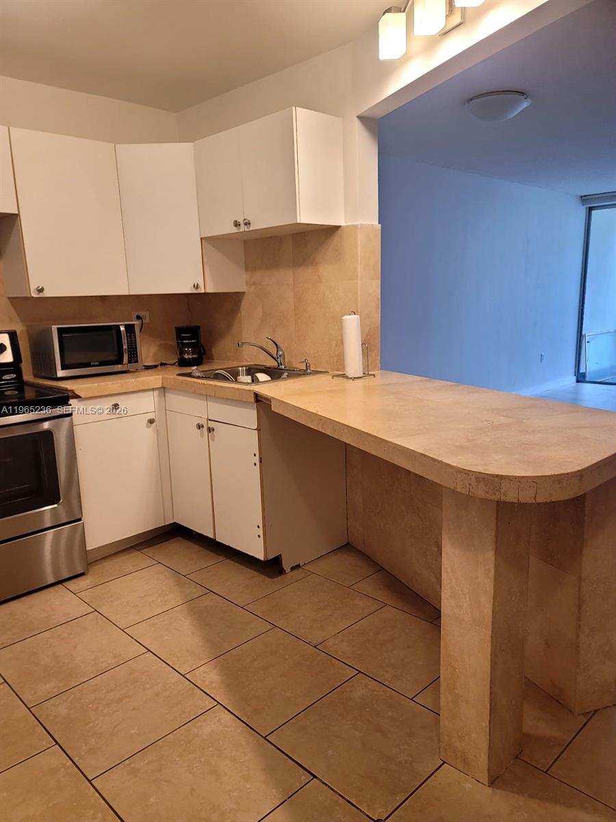 A kitchen features white cabinets, stainless steel appliances, and a beige stone breakfast bar — 1690 NE 191st St # 1, Miami FL 33179, MIAMI, FL