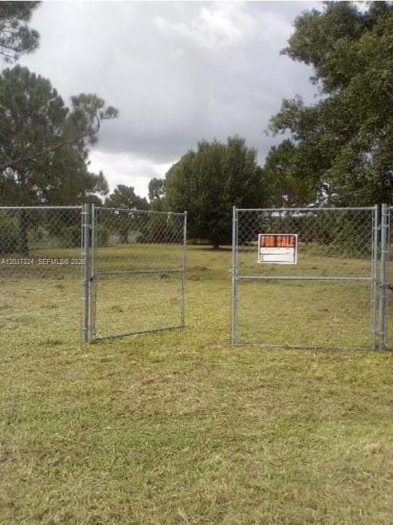 A chain-link fence with an open gate surrounds a grassy, tree-lined vacant lot — 460 Horse Club Ave, Clewiston FL 33440, CLEWISTON, FL