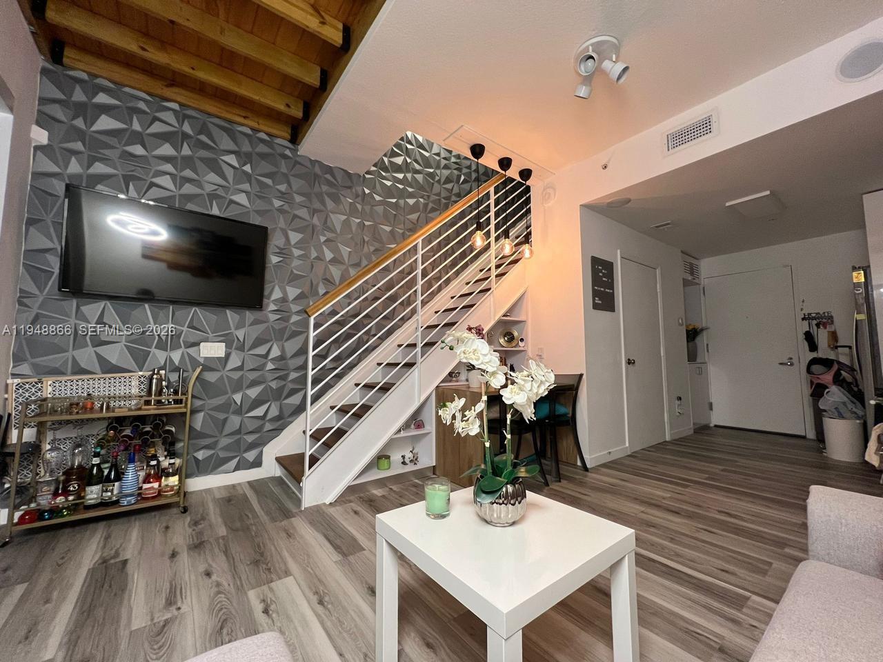 A living room features a textured gray accent wall, a staircase, and wood-look flooring — 60 SW 13th St # 3013, Miami FL 33130, MIAMI, FL